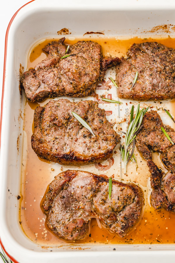 baked lamb in a baking dish garnished with rosemary leaves.