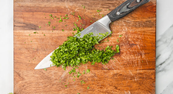 chopped herbs on a knife on a chopping board.