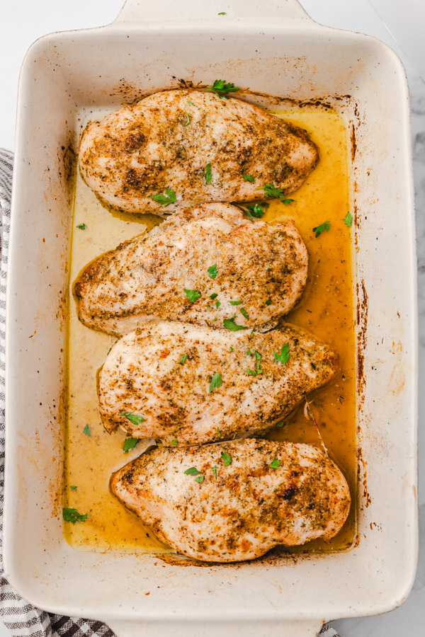 four baked chicken breasts in a baking dish.