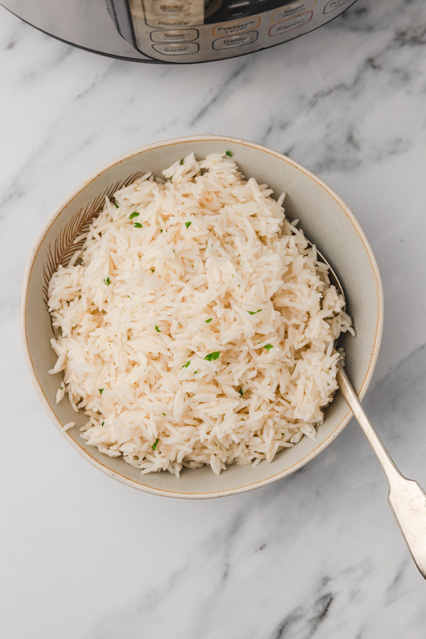 a bowl of garlic rice with spoon in front of an instant pot.