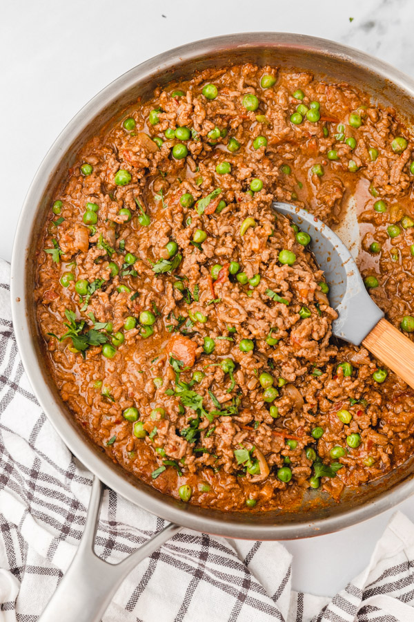 ground beef curry and peas in a skillet with a silicon spatula.