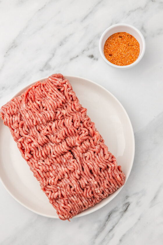 raw ground beef placed beside a small pot of seasoning.