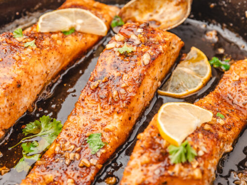 three salmon fillets covered in shiny glaze in a cast iron skillet.