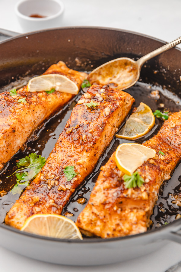 three salmon fillets covered in shiny glaze in a cast iron skillet.
