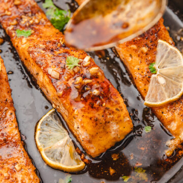 sticky sauce on a spoon drizzling over salmon fillets in a skillet.