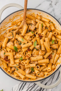 a skillet of marry me chicken pasta garnished with fresh baby basil leaves.