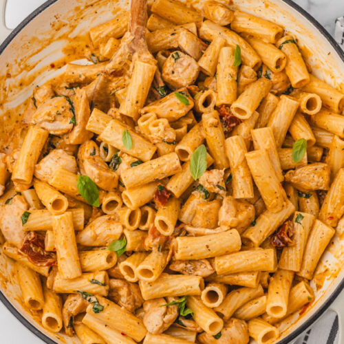 a skillet of marry me chicken pasta garnished with fresh baby basil leaves.