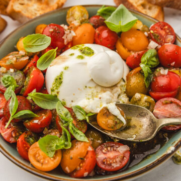 tomato burrata salad with a spoon on a plate.