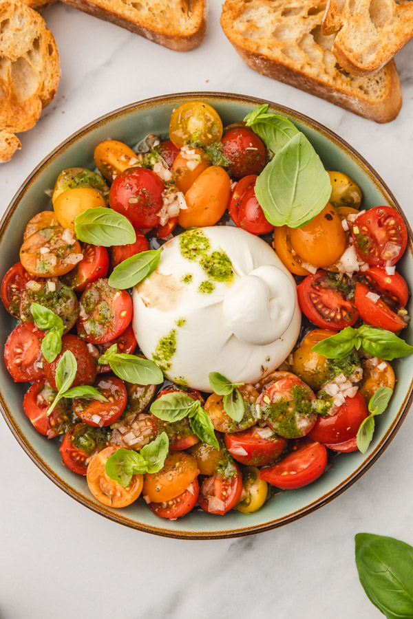 a bowl of tomato salad and burrata garnished with fresh baby basil leaves.