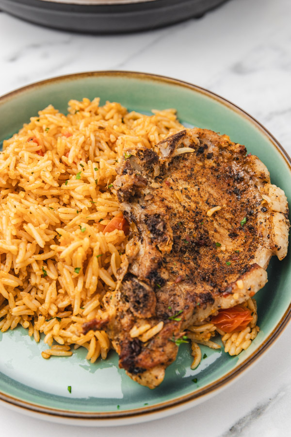 a plate tomato rice and bone in pork chops.