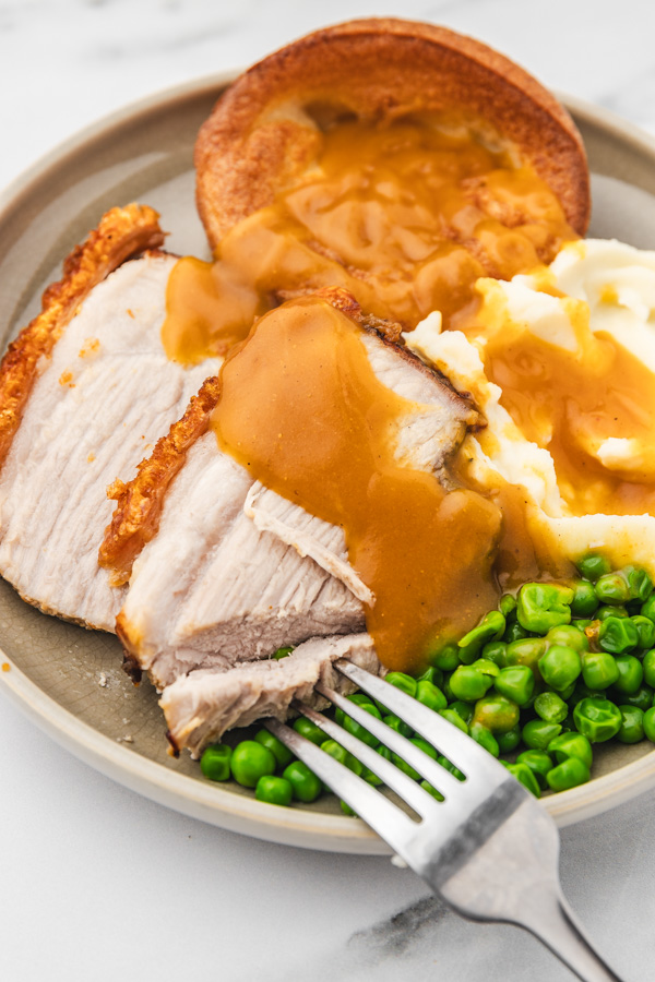 a plate of pot roast with mash, peas, yorkshire pudding ang gravy.