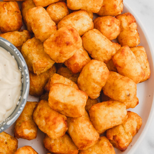 a plate of golden brown tater tots with a side of dipping sauce.