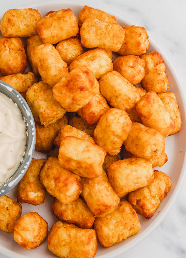 a plate of golden brown tater tots with a side of dipping sauce.