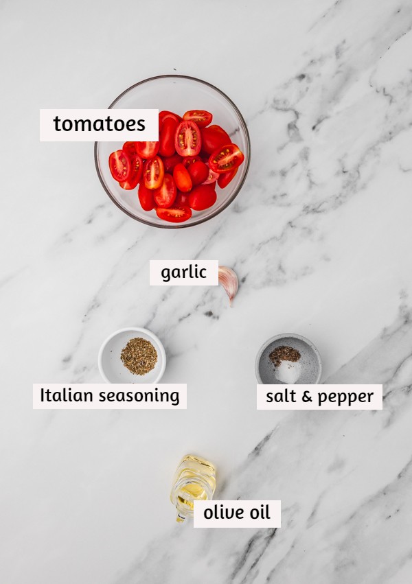 the ingredients for making roasted tomatoes laid on a white marble surface.