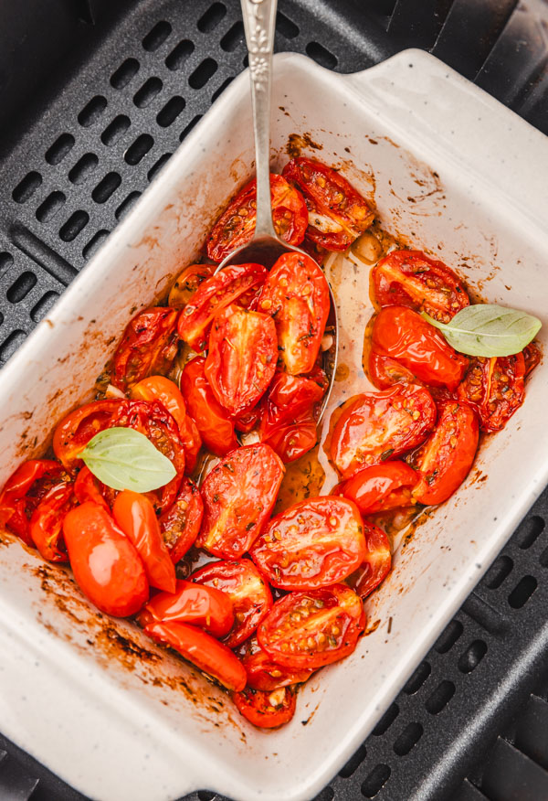 roasted tomatoes in a baking dish in an air fryer basket.