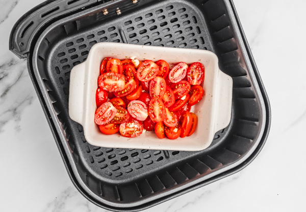 sliced tomatoes in a baking dish placed in air fryer basket.