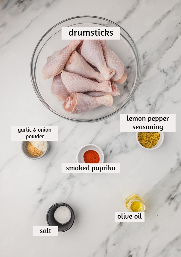 ingredients for lemon pepper chicken drumsticks laid on a white marble surface.