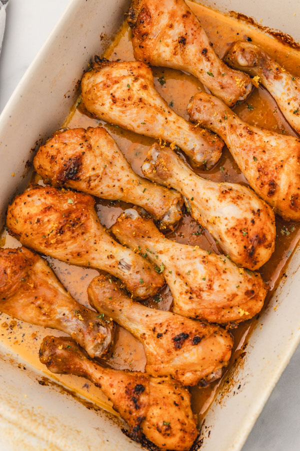 eleven cooked chicken legs in a baking dish.