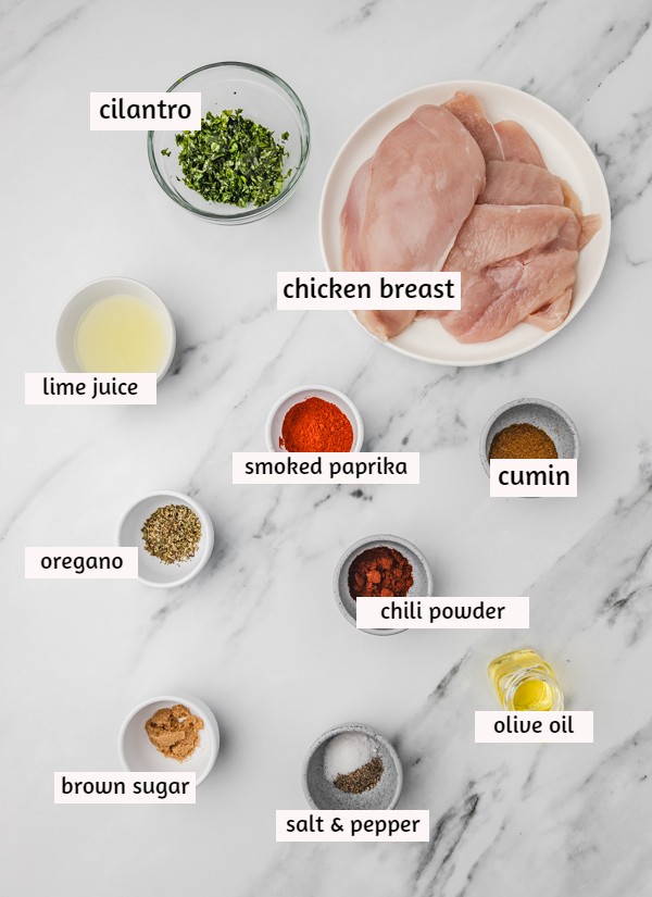 ingredients to make mexican chicken on a white marble surface.