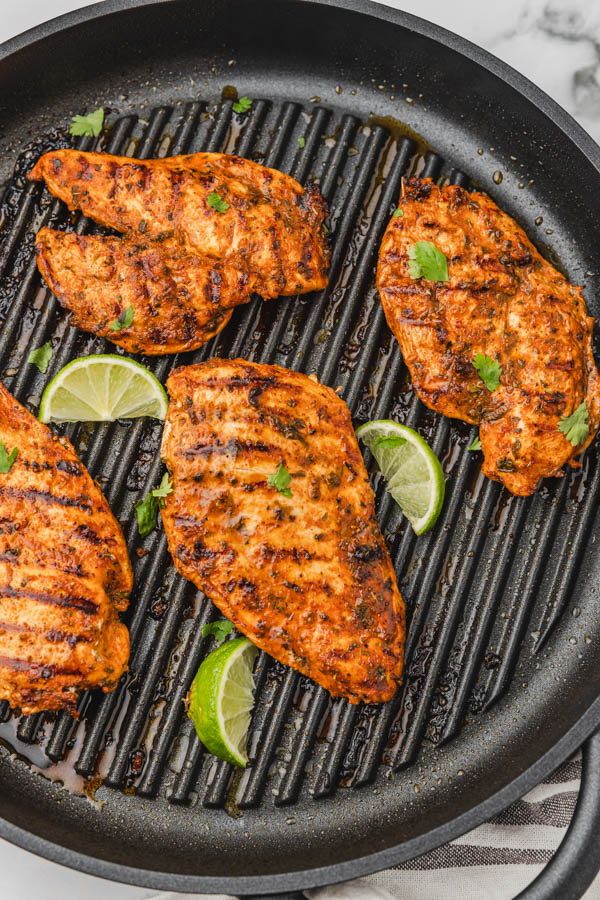 four pan grilled chicken in a griddle pan with lime wedges.