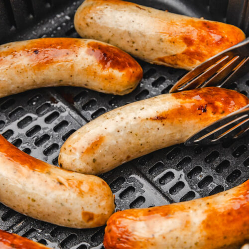 six cooked brats in air fryer basket.