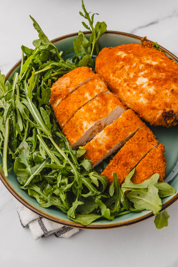 a plate of breaded chicken breast and rocket salad.