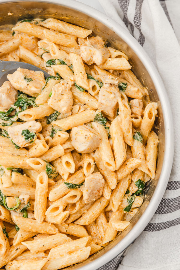 creamy penne pasta in a skillet placed beside a white napkin.