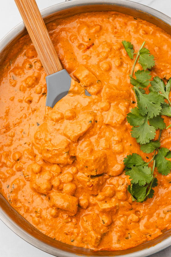 creamy curry in a skillet garnished with fresh cilantro leaves.