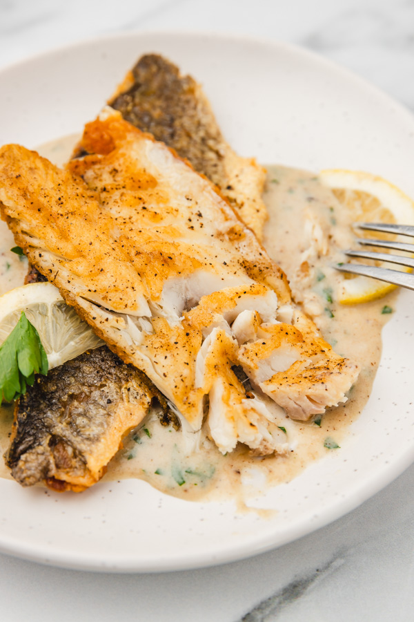 a plate of sea bass fillets showing the fleshy part flaked with a fork.