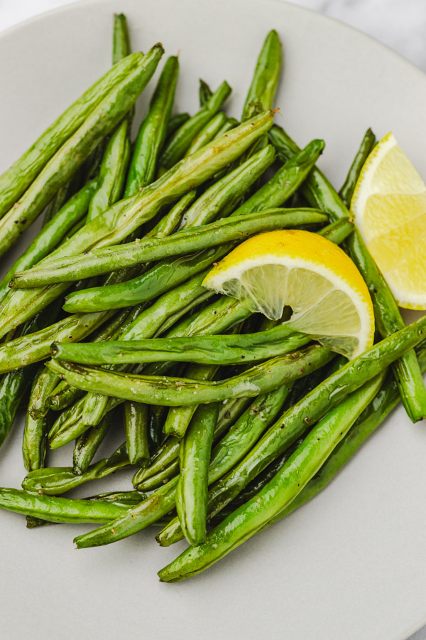 close up of green beans in a plate with two lemon wedges.