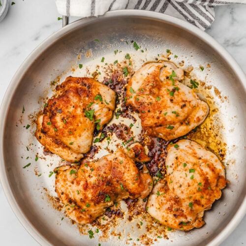 four pan fried chicken thighs in a skillet.