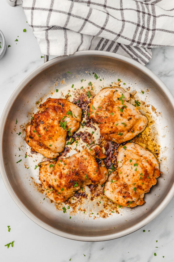 four pan fried chicken thighs in a skillet.