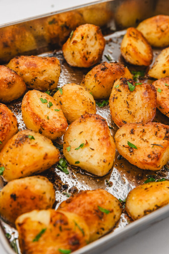 crispy potatoes garnished with chopped rosemary and parsley in a roasting pan.