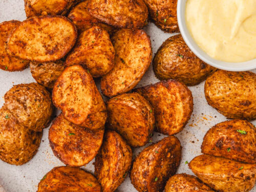 a bowl of seasoned potatoes with a small bowl of dipping sauce placed beside it.