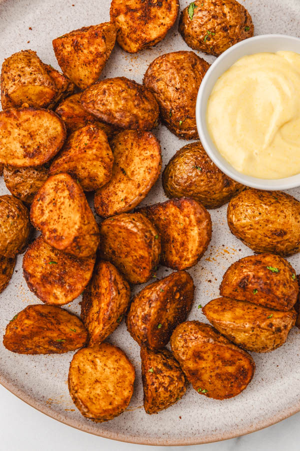 a close up of cajun potatoes in a flat plate with dipping sauce.