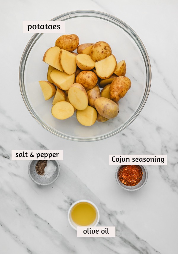 ingredients needed to make cajun potatoes on a white marble surface.