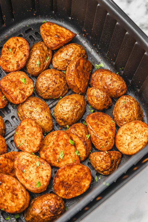 cooked potatoes garnished with parsley in an air fryer basket.