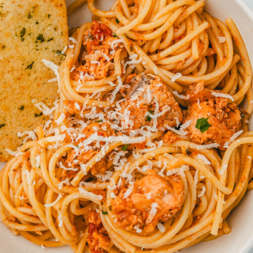 a bowl of salmon pasta with garlic bread.