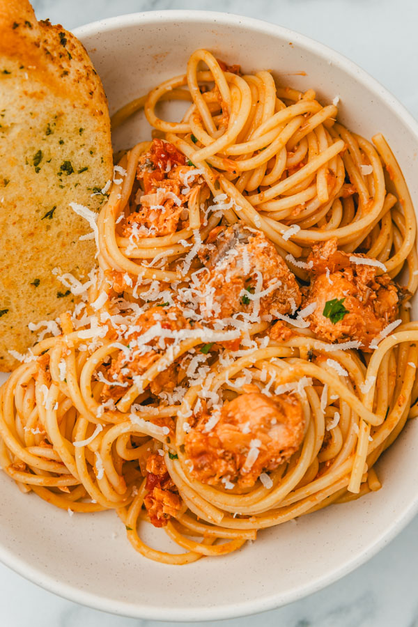 a close up of spaghetti in a bowl with garlic bread.