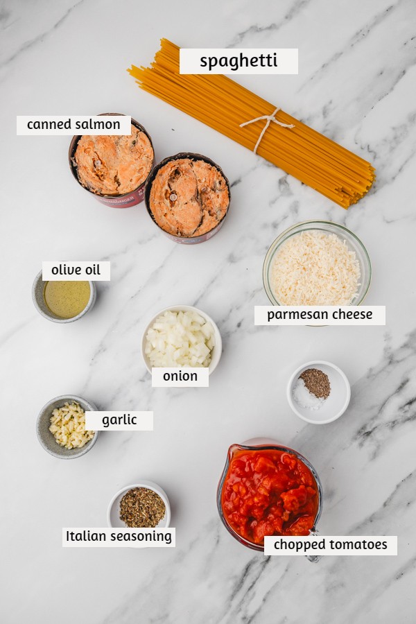 ingredients needed to make canned salmon pasta laid on a white marble surface.