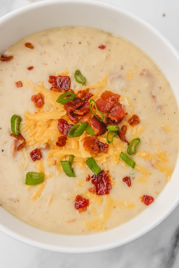 a bowl o potato soup topped with cheddar cheese, bacon and green onions.