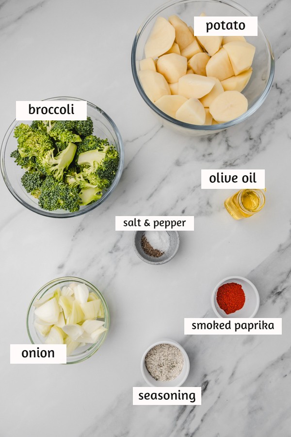 ingredients to cook broccoli and potatoes on a white marble surface.