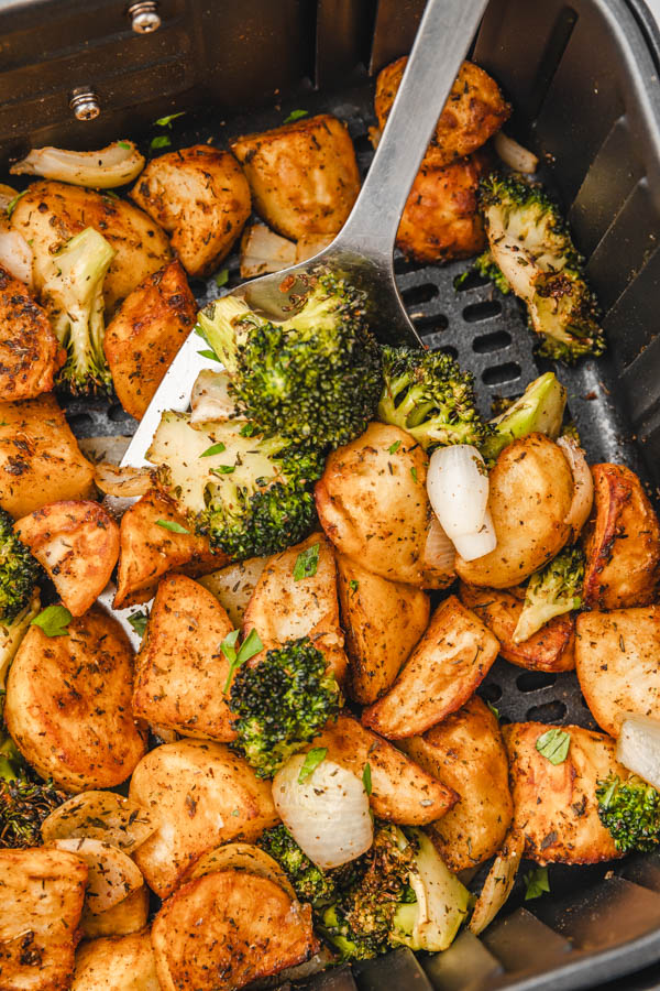 spatula in air fryer basket with broccoli and potatoes.