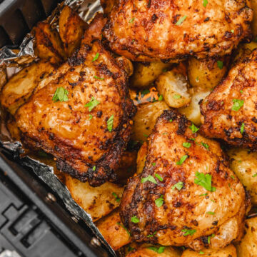 chicken thighs and potatoes garnished with fresh parsley in an air fryer basket.
