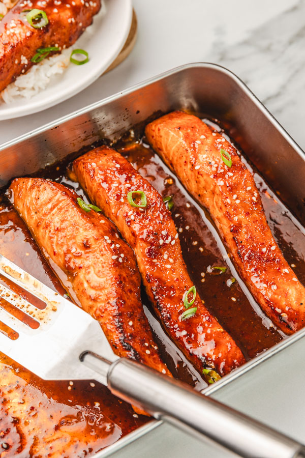 salmon in a sticky sauce in a baking dish with fish spatula.