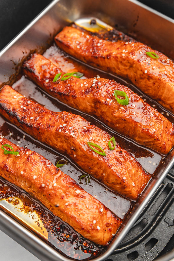 four salmon fillets in a sticky sauce garnished with sesame seeds and chopped green onions.