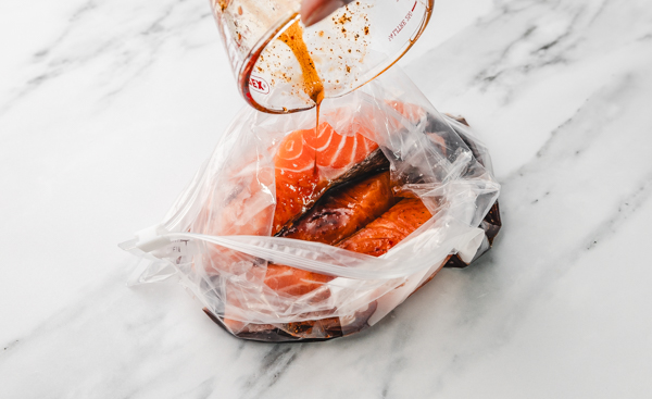 pouring marinade over salmon fillets in a ziploc bag.
