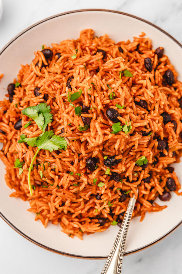 a plate of mexican red rice and beans with spoon.