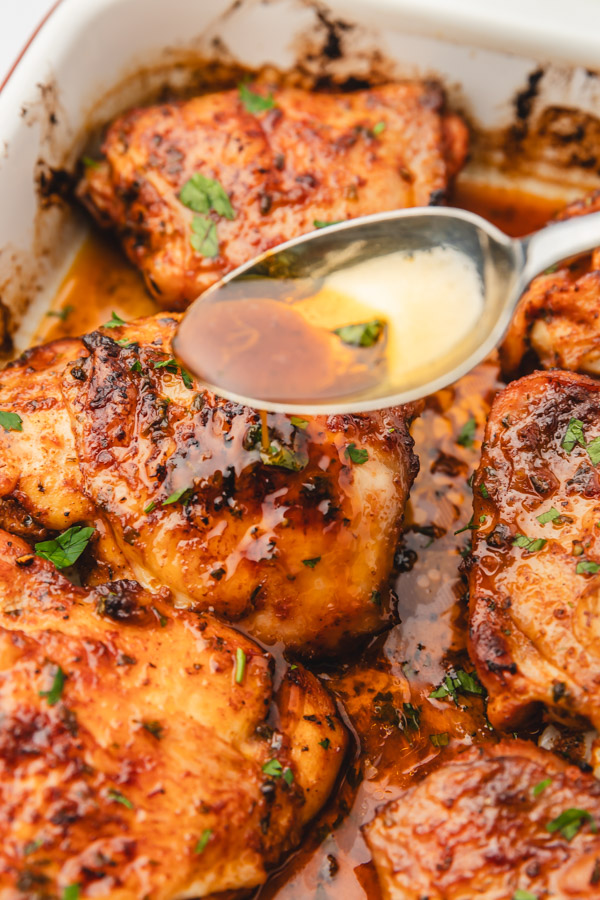 a hand spoon sauce on a chicken thigh.