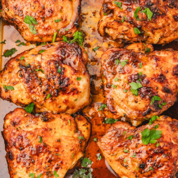 chicken thighs garnished with parsley in a baking sheet.